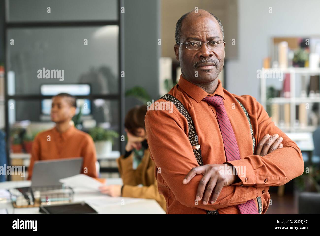 Portrait vers le haut de la taille d'un homme senior noir confiant posant dans le bureau debout avec les bras croisés et regardant l'appareil photo avec l'espace de copie d'expression sérieuse Banque D'Images
