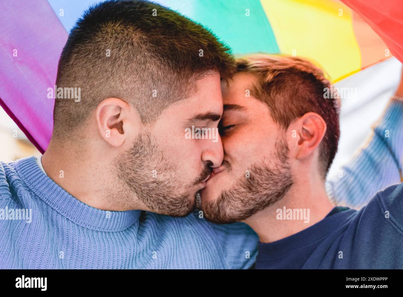 Couple masculin gay s'embrassant sous le drapeau lgbtq arc-en-ciel pendant le défilé du mois de la fierté. Concept de relation amoureuse Banque D'Images