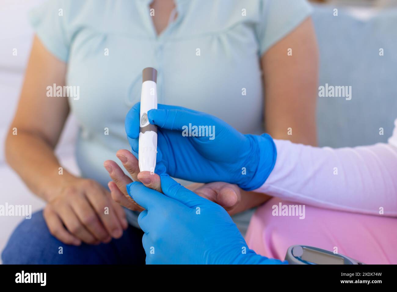 Infirmière en gants bleus contrôlant la glycémie d'une femme âgée à domicile Banque D'Images