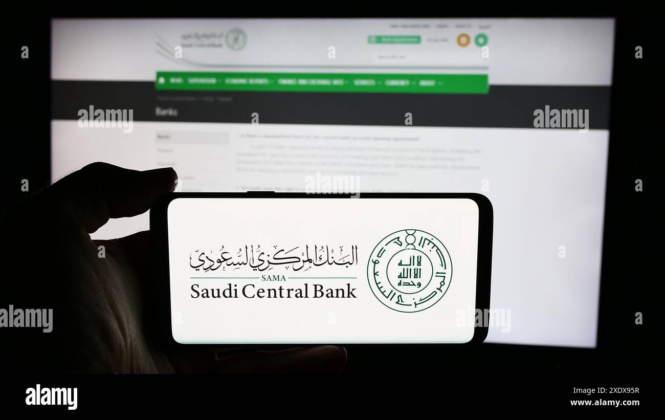 Personne tenant un téléphone portable avec le logo de l'institution financière Saudi Central Bank (SAMA) en face de la page Web. Concentrez-vous sur l'affichage du téléphone. Banque D'Images