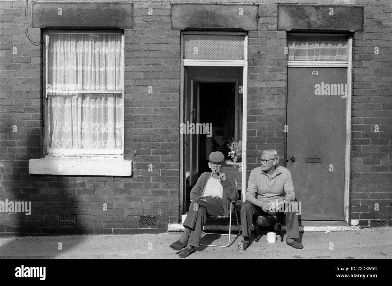 Village de puits communauté minière de charbon Yorkshire années 1970 Nord de l'Angleterre. Deux mineurs sur leur jour de congé, assis à l'extérieur de leurs maisons mitoyennes sur le trottoir profitant d'un homme au soleil. South Kirkby, Yorkshire Angleterre 1979. ANNÉES 1970 ROYAUME-UNI HOMER SYKES Banque D'Images