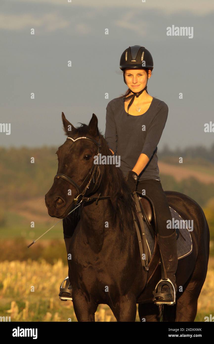 Fille sur le dos d'un poney pendant le coucher du soleil Banque D'Images