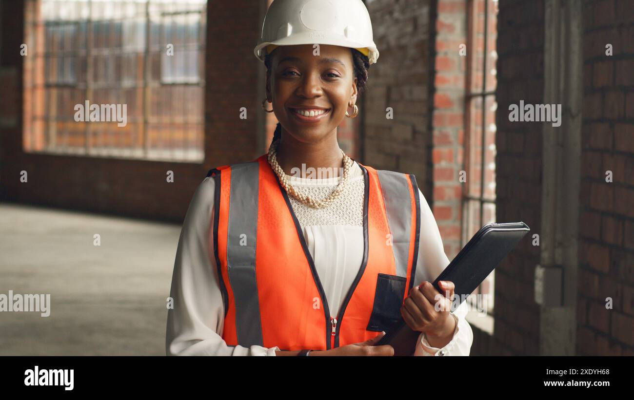 Ingénieur confiant sur le chantier de construction tenant une tablette et portant un équipement de sécurité Banque D'Images