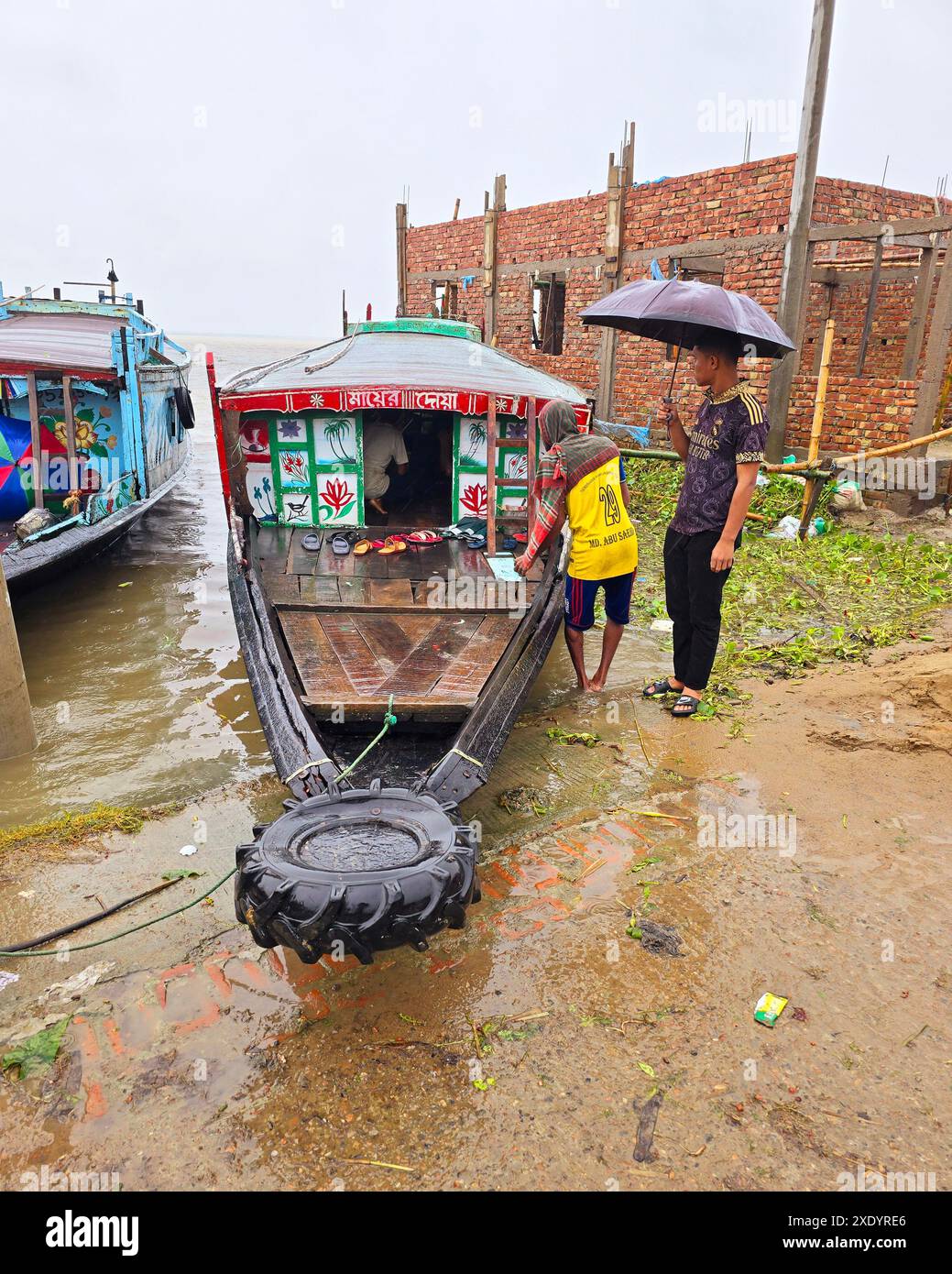 Passagers embarquant et débarquant, sous la pluie tropicale, de lancers de pays qui sont amarrés sur la rive de Dingapotha, Mohonganj «haor» (un grand corps de zone humide formé par la rivière et l'eau de pluie, célèbre comme zone de pêche). Netrokona, Bangladesh. Banque D'Images