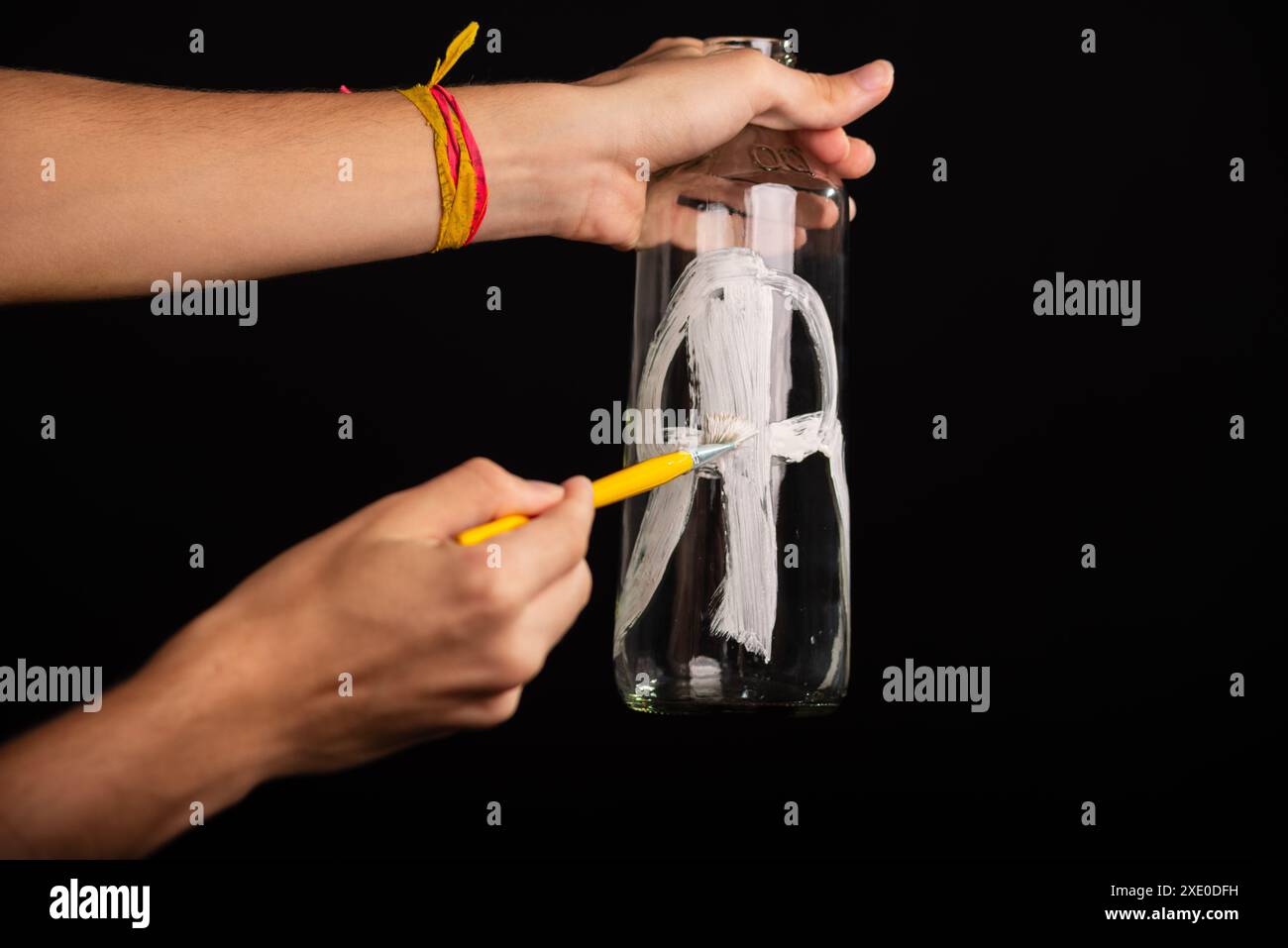 Un artiste tenant et peignant une bouteille en verre avec de la gouache rouge et blanche noire. Isolé sur fond noir. Banque D'Images