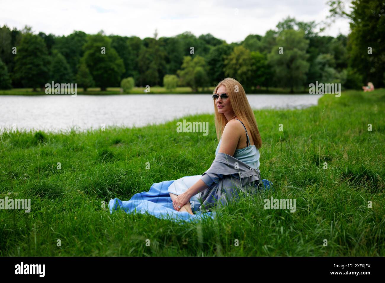 Une femme se détache sur une couverture au bord du lac, entourée d'herbe verte Banque D'Images