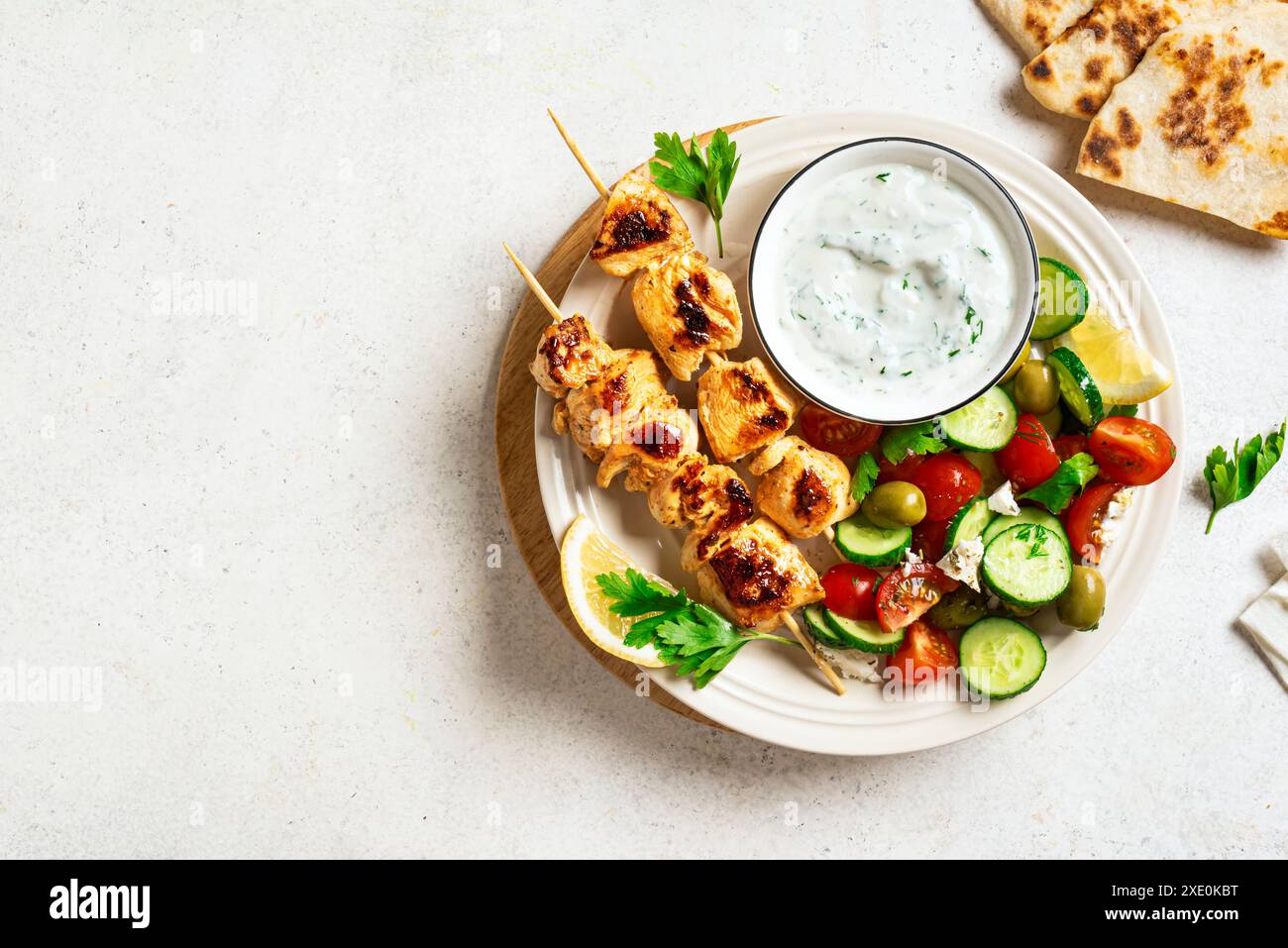 Kebab de poulet grillé avec salade de légumes frais sur fond blanc, vue de dessus, espace de copie. Déjeuner méditerranéen avec brochettes rôties, sauce tzadziki A. Banque D'Images