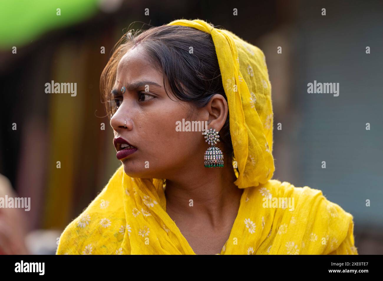 Jeune femme indienne tête et épaules en foulard jaune et boucles d'oreilles saree argentées regardant vers sa droite Banque D'Images