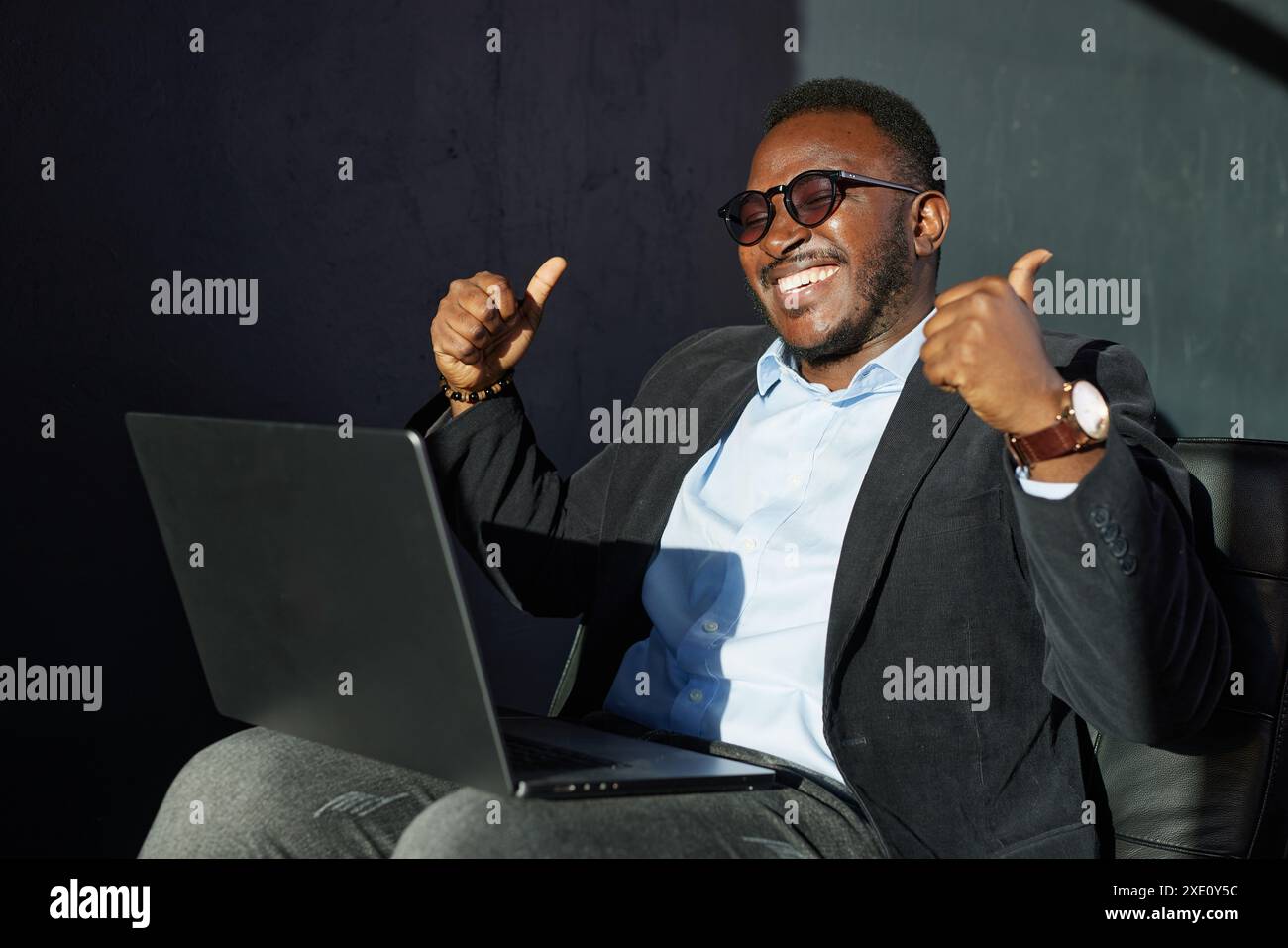 Heureux homme d'affaires africain avec ordinateur portable montrant les pouces vers le haut excellent signe sur fond sombre, homme d'affaires réussi Banque D'Images