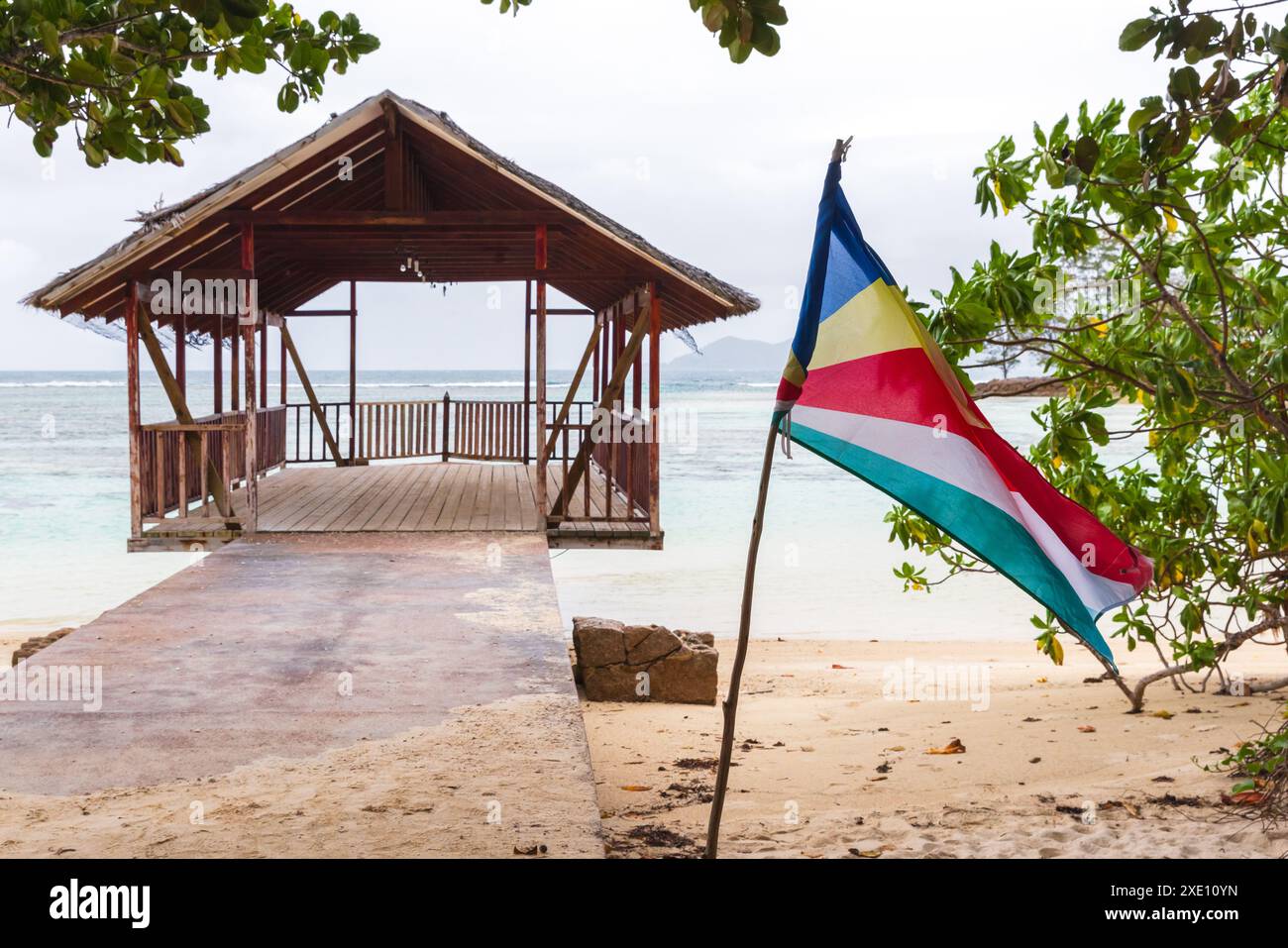 Île de la Digue, Seychelles. Anse Union paysage de plage avec drapeau et un gazebo vide à la jetée sur le fond Banque D'Images