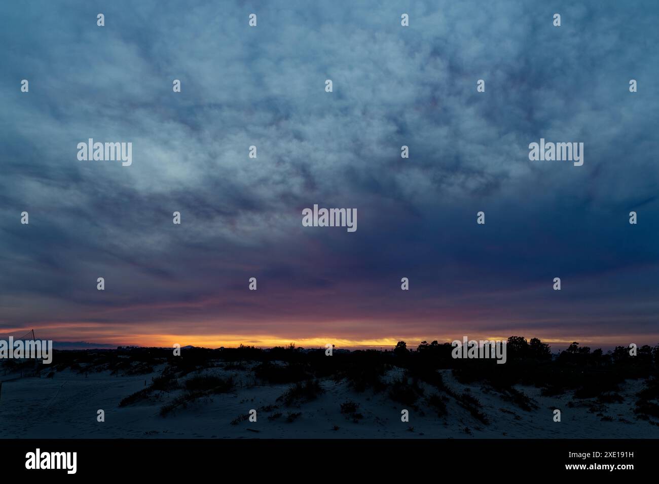 Coucher de soleil au Portugal avec des teintes vibrantes se propageant dans le ciel, créant un contraste avec le paysage sombre Banque D'Images