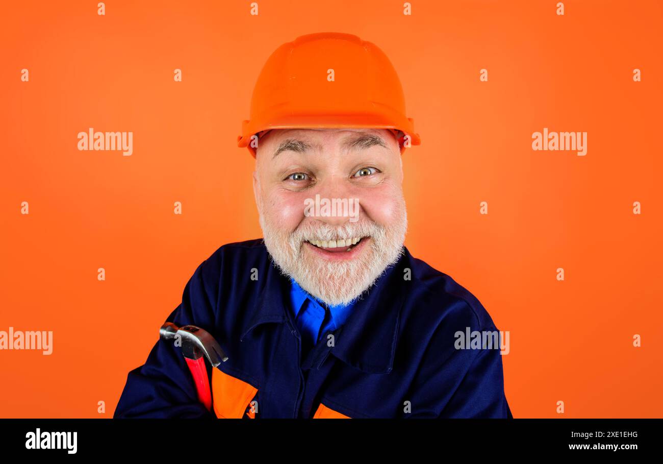 Homme barbu souriant dans le casque de construction et uniforme avec marteau. Industrie du bâtiment. Gros plan portrait de beau constructeur, réparateur, charpentier dans Banque D'Images