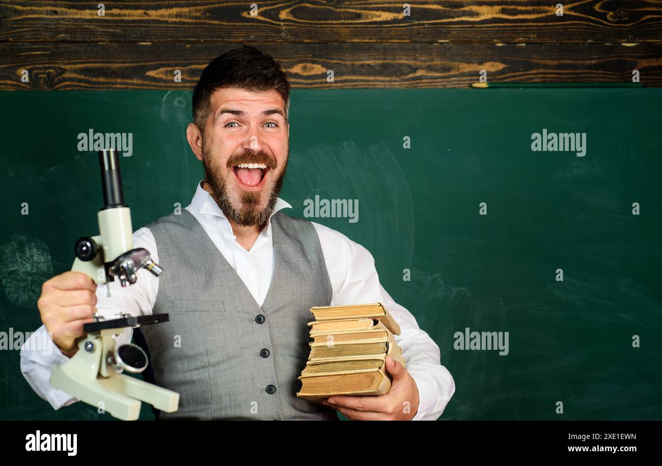 Leçon de chimie ou de biologie. Heureux professeur ou étudiant avec des livres et microscope dans la salle de classe près du tableau noir. Travaux pratiques en chimie. Recherche Banque D'Images
