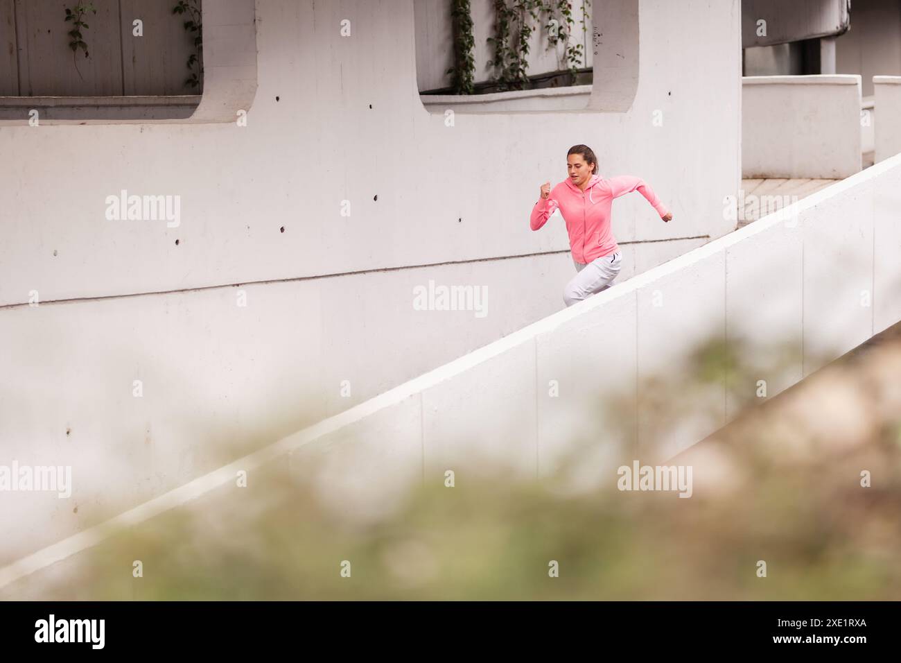 Une jeune femme motivée est capturée en train de courir énergiquement sur des structures en béton blanc dans un environnement urbain, portant des vêtements de sport rose vif. Banque D'Images
