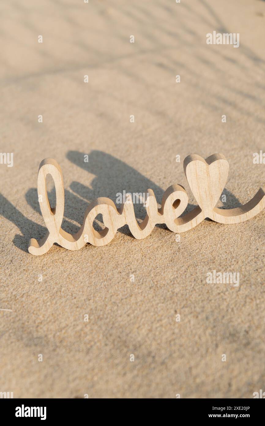 Mot en bois amour sur fond de plage de sable. Concept d'anniversaire de vacances romantique, proposition, carte de voeux de Saint Valentin, pos Banque D'Images