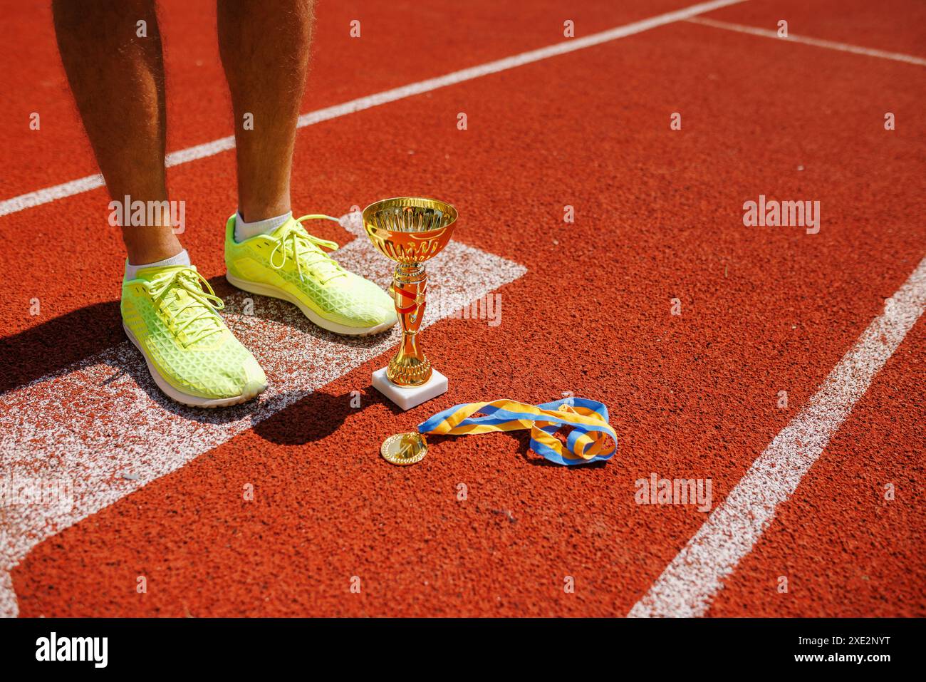 Un athlète triomphant avec un trophée sur le terrain d'athlétisme, ses jambes, une coupe et une médaille pour la première place close-up, le concept de victoire dans le sport Banque D'Images