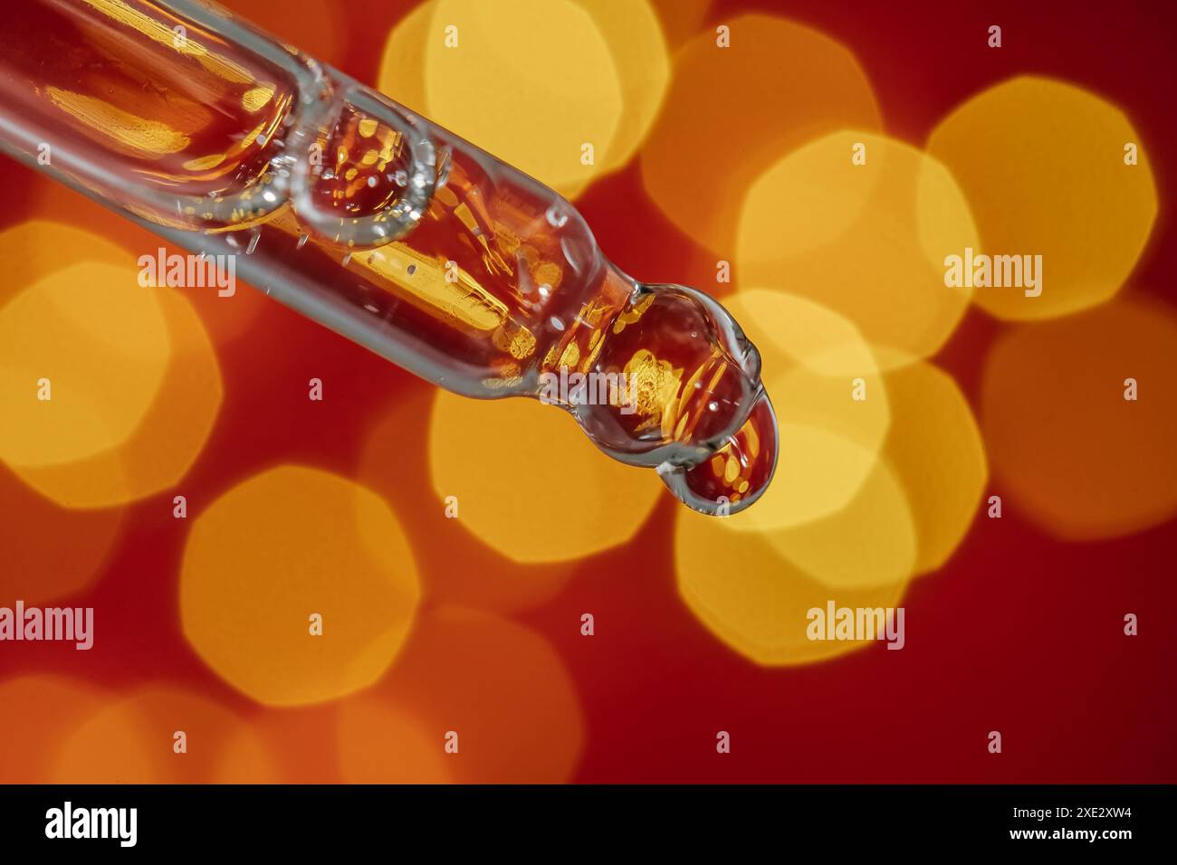 Pipeter avec du sérum sur un fond rouge de vacances avec du bokeh. Banque D'Images