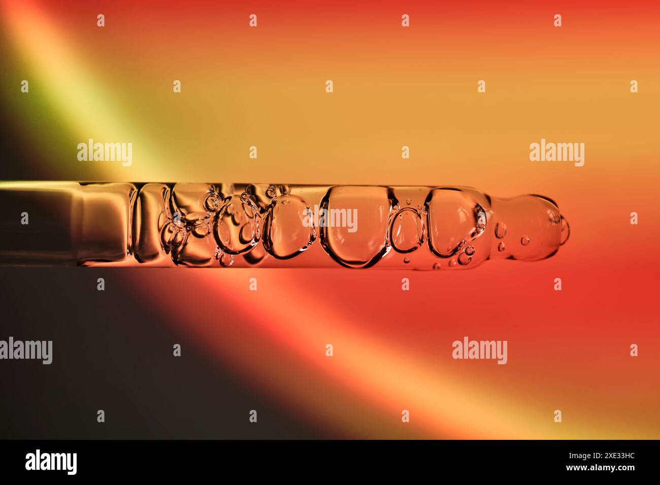 Un compte-gouttes avec sérum corporel de crème solaire dans la lumière du coucher de soleil orange. Banque D'Images