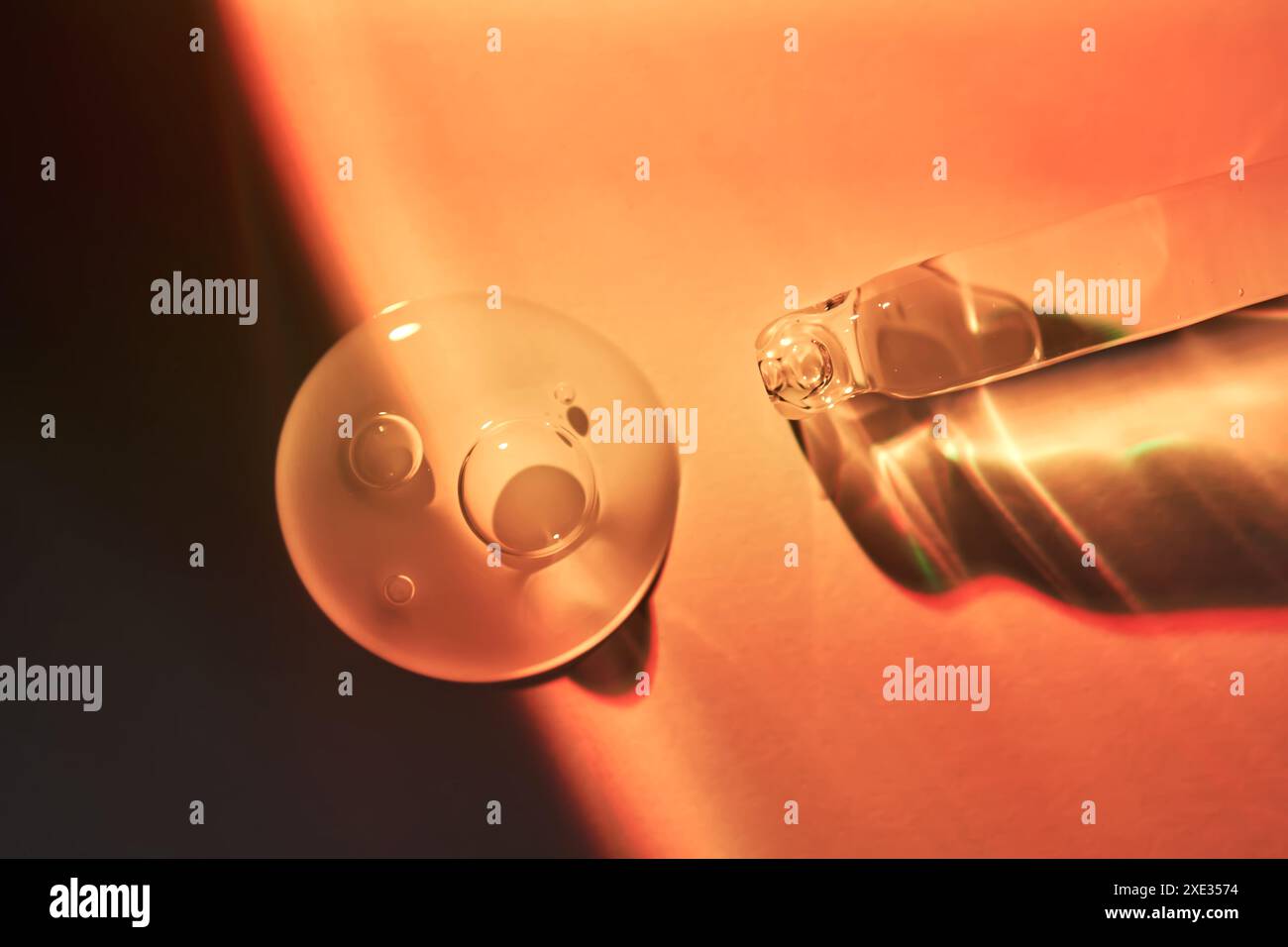 Un compte-gouttes et une goutte de sérum corporel de protection solaire dans la lumière orange du coucher du soleil. Banque D'Images