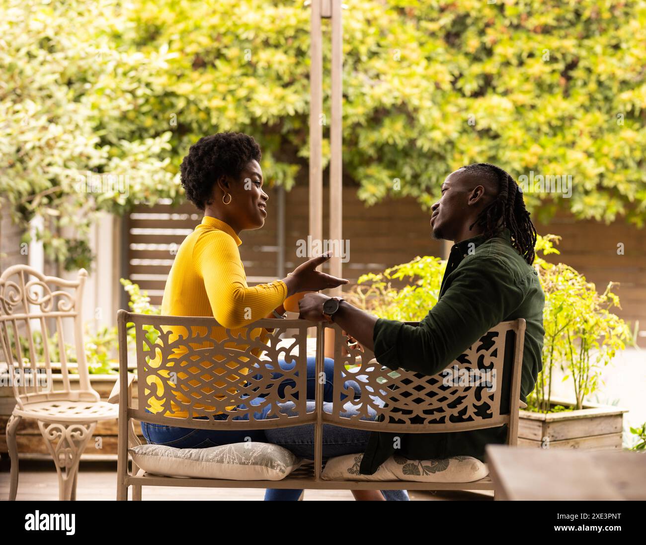 Couple afro-américain assis sur le banc, souriant et parlant dans le jardin Banque D'Images