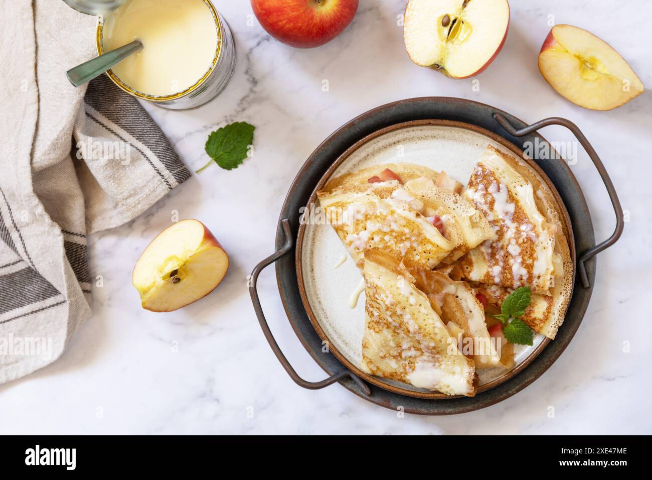 Célébration de la journée des crêpes, petit déjeuner sain. Crêpes sucrées maison avec pommes et lait condensé sur une table en marbre. Vue de dessus Banque D'Images