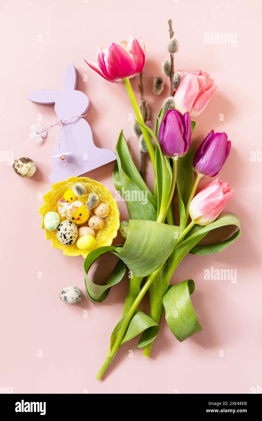 Tulipes roses et violettes avec des œufs de caille colorés dans un nid sur fond rose. Concept de vacances de printemps et de Pâques. Vue de dessus à plat Banque D'Images