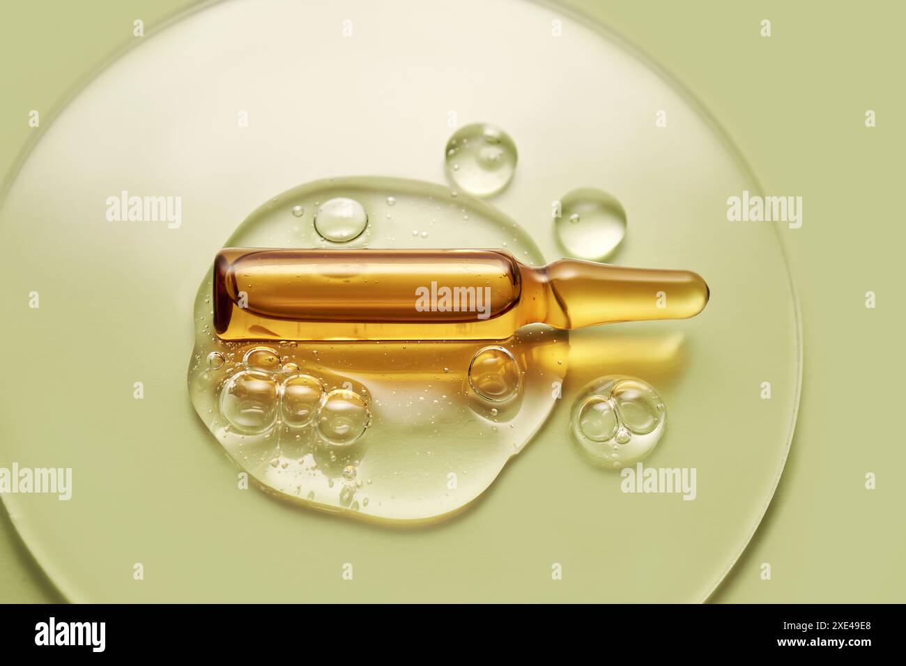 Ampoule dans une goutte de gel cosmétique sur un fond vert. Banque D'Images