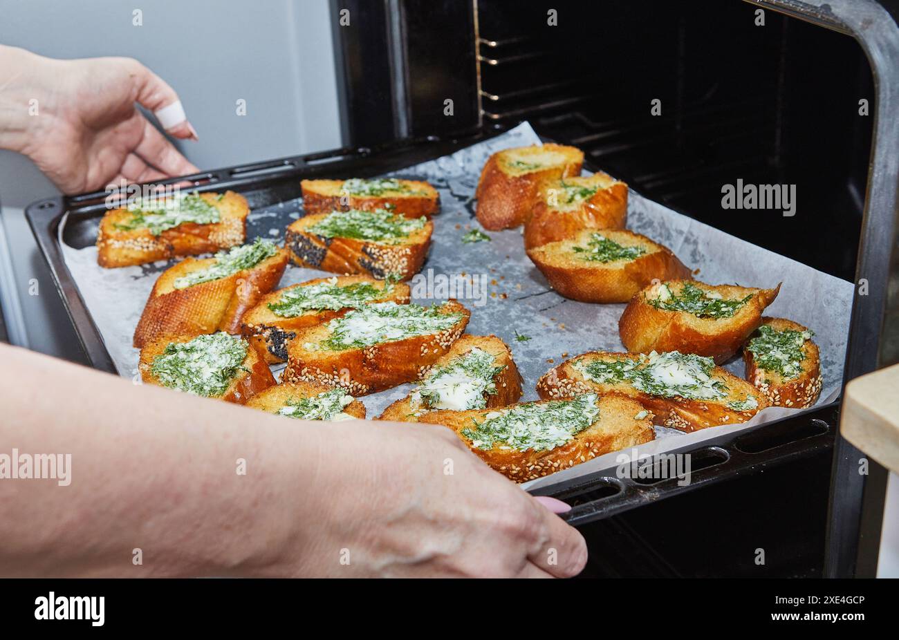 Mains placer une plaque de cuisson de pain à l'ail fraîchement préparé avec des herbes et du beurre dans le four. Banque D'Images