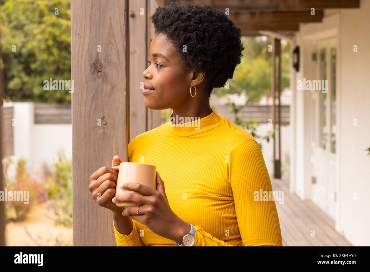 Femme tenant une tasse à café, debout sur le porche, regardant soigneusement dans la distance Banque D'Images