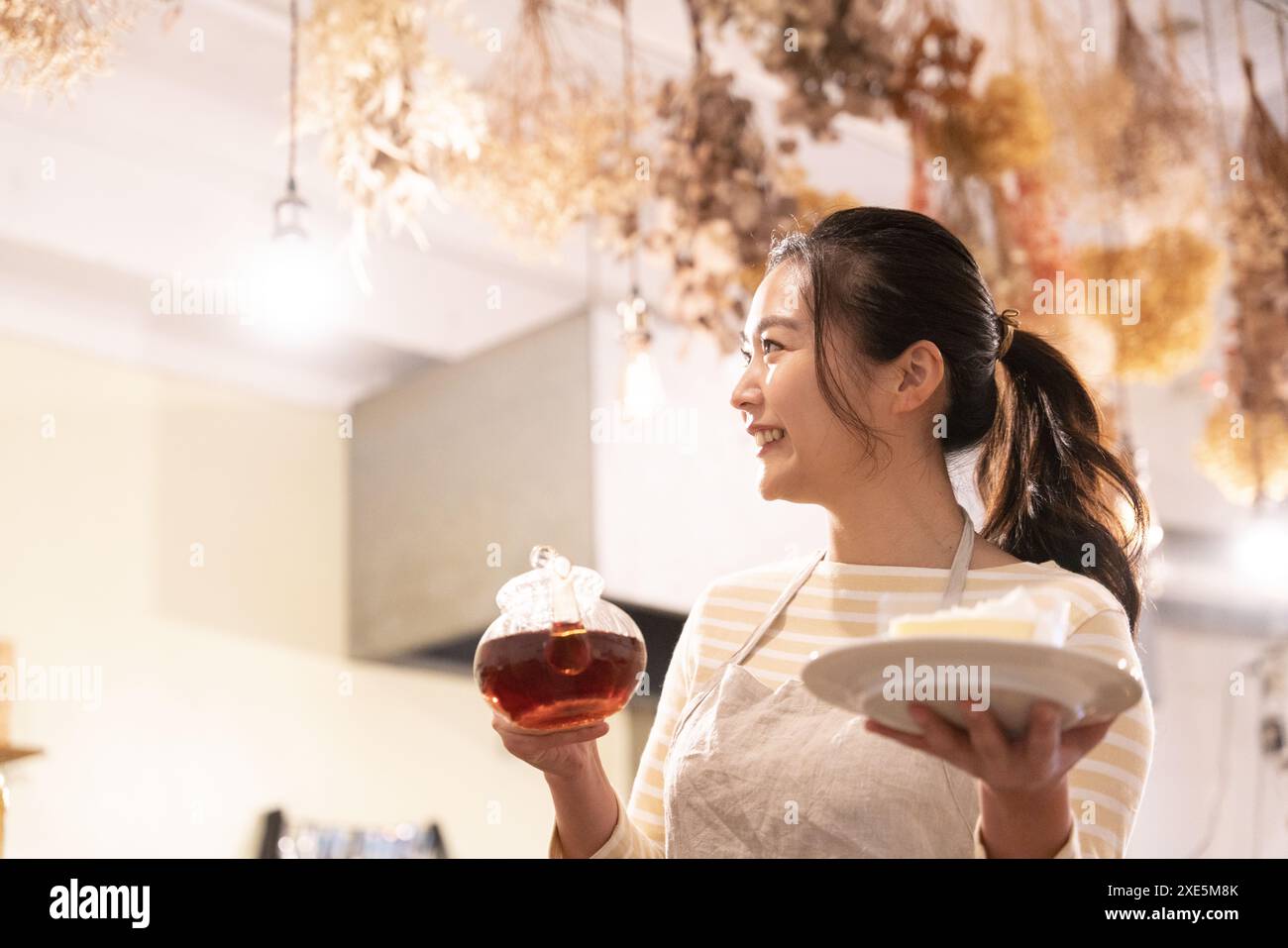 Assistante de magasin tenant une théière et un gâteau dans un café Banque D'Images