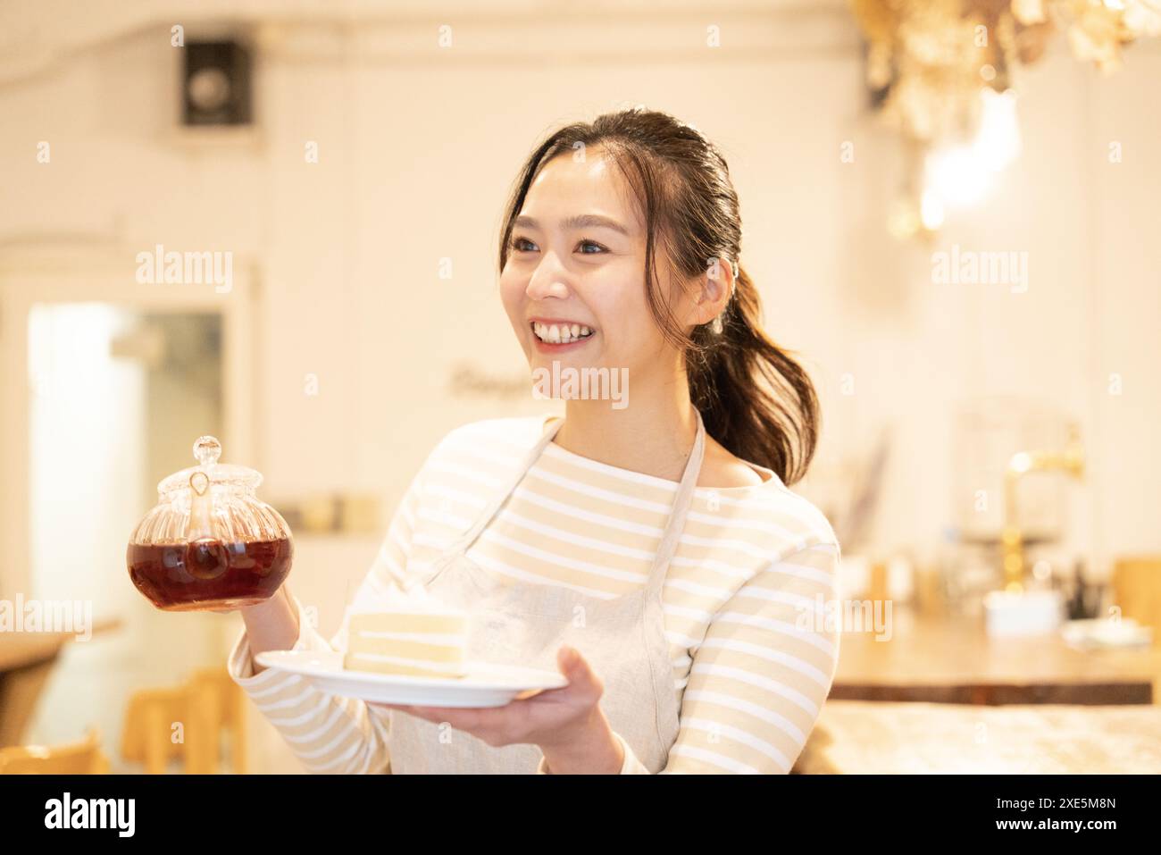 Femme tenant gâteau et théière au café Banque D'Images