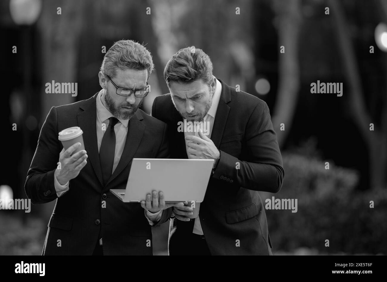 Équipe d'hommes d'affaires utilisant un ordinateur portable à l'extérieur. Collègues en costume parlant à l'extérieur. Les hommes d'affaires discutent de l'extérieur. Deux hommes d'affaires parlent de stratégie de projet Banque D'Images