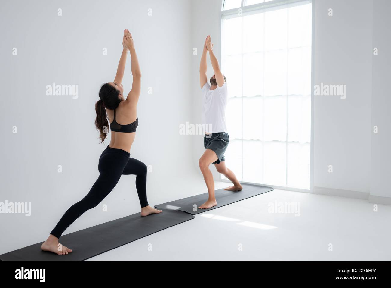 Jeune couple pratiquant le yoga dans une salle blanche de studio. Banque D'Images