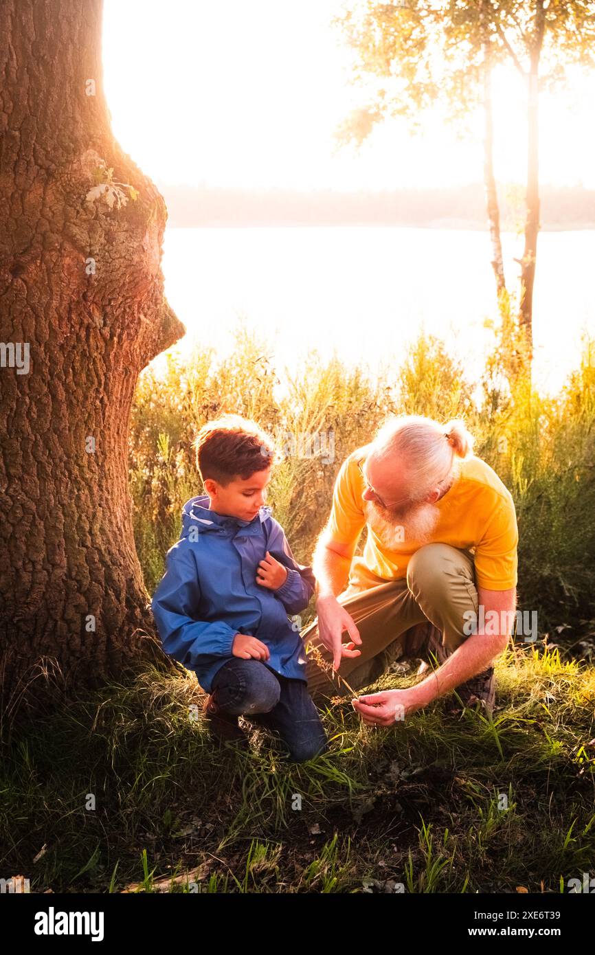 Grand-père enseignant petit-fils près du lac au crépuscule Banque D'Images