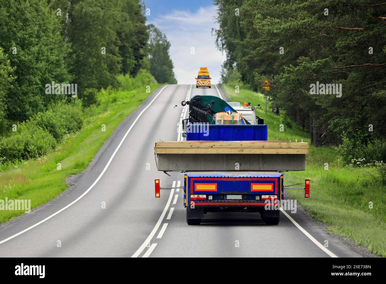 Camion lourd et remorque transportant une charge large sur l'autoroute avec le véhicule pilote devant. Vue arrière, espace de copie. Banque D'Images