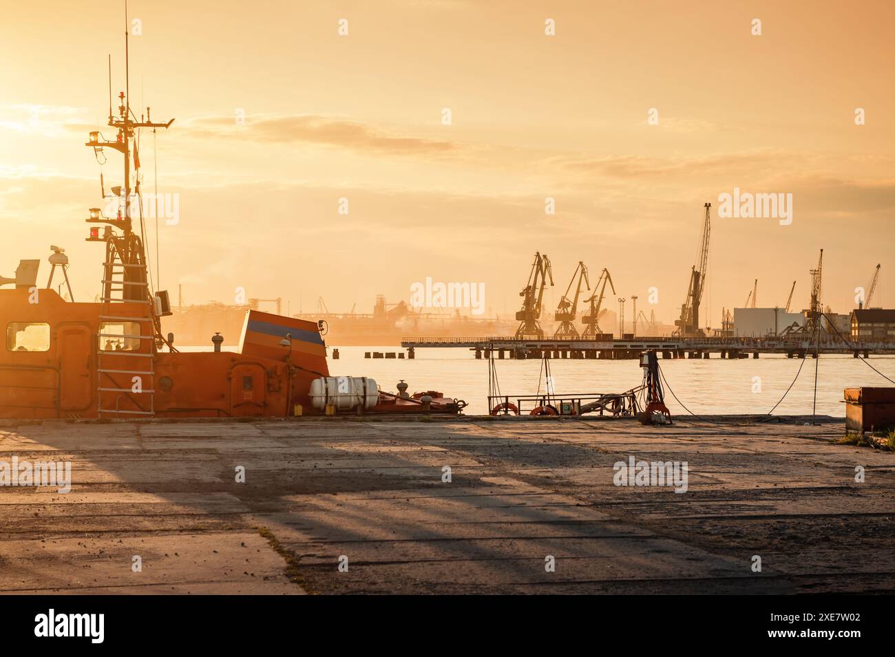 Coucher de soleil au port. Bateau pilote rouge amarré par la jetée et beaucoup de grues en arrière-plan Banque D'Images