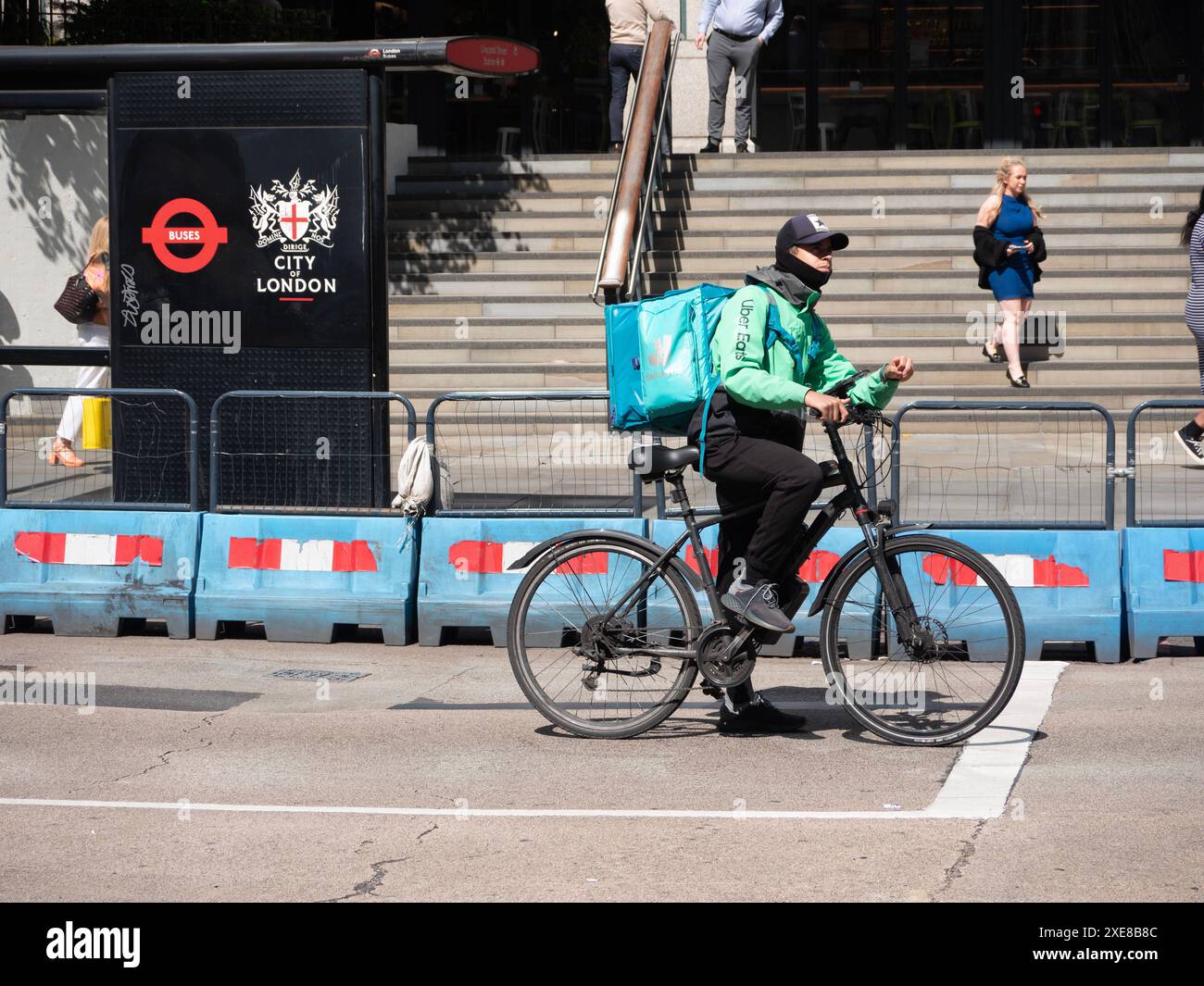Le coureur de livraison de nourriture double agent portant la veste Uber Eats avec sac à dos Deliveroo attend à la jonction à Bishopsgate, à côté du panneau City of London Banque D'Images