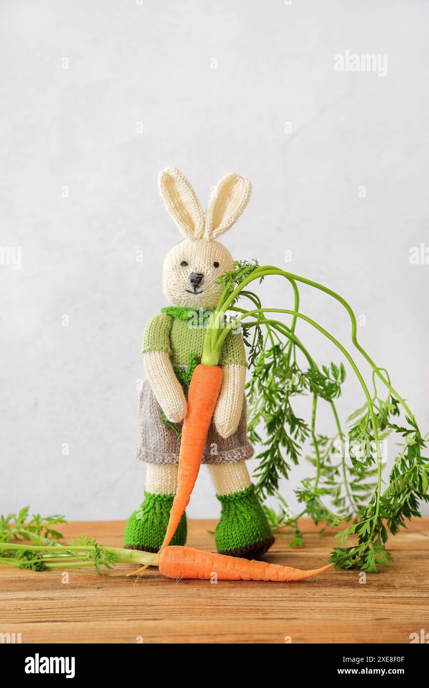 Lapin mignon tricoté debout sur une table en bois tenant une carotte fraîche avec espace de copie Banque D'Images