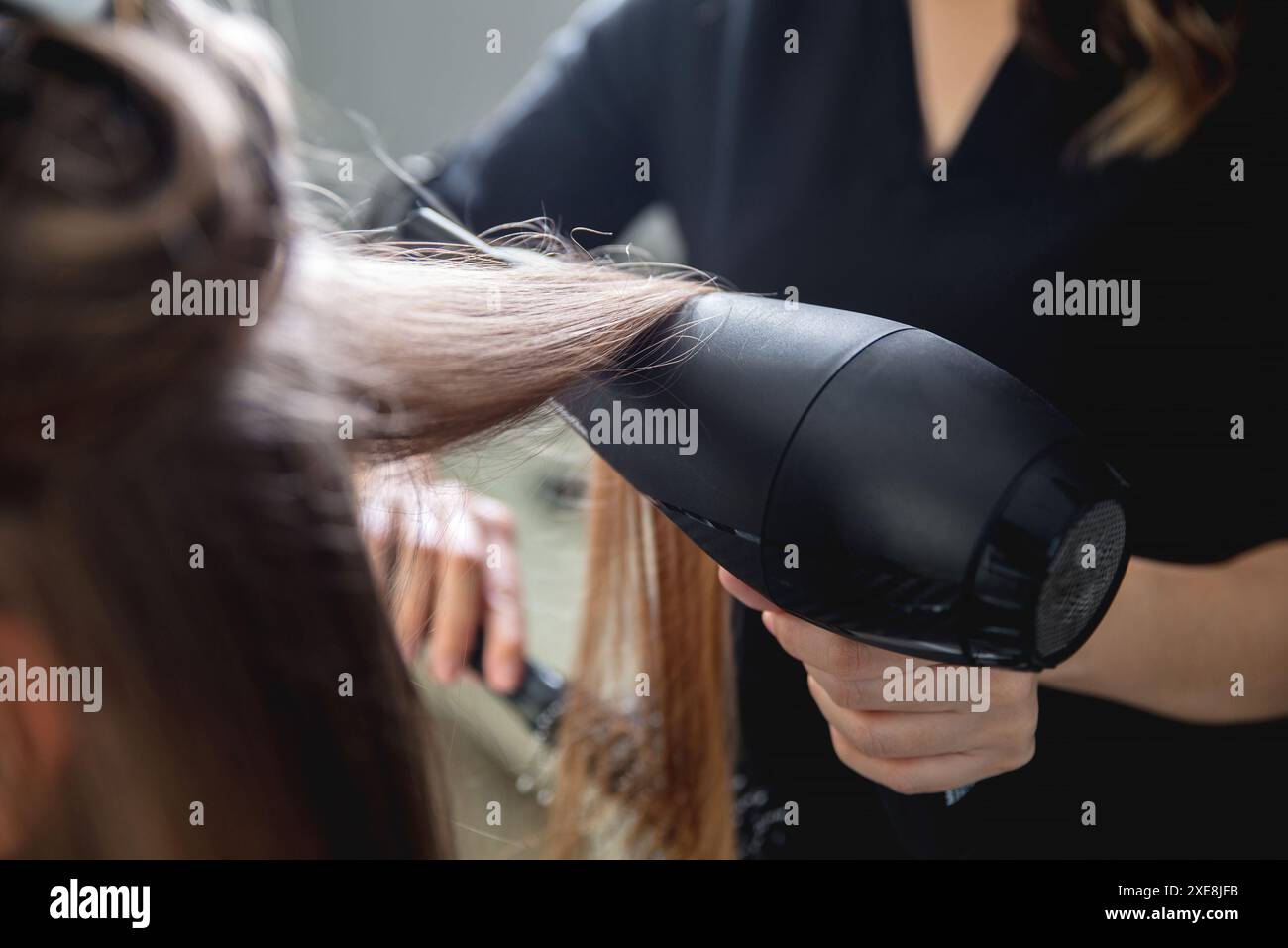 Gros plan des mains de coiffeurs séchant de longs cheveux blonds avec sèche-cheveux et brosse ronde Banque D'Images