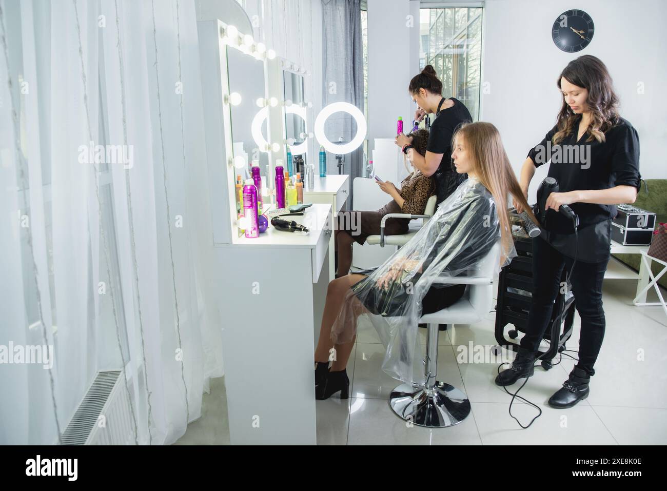 Gros plan des mains de coiffeurs séchant de longs cheveux blonds avec sèche-cheveux et brosse ronde Banque D'Images