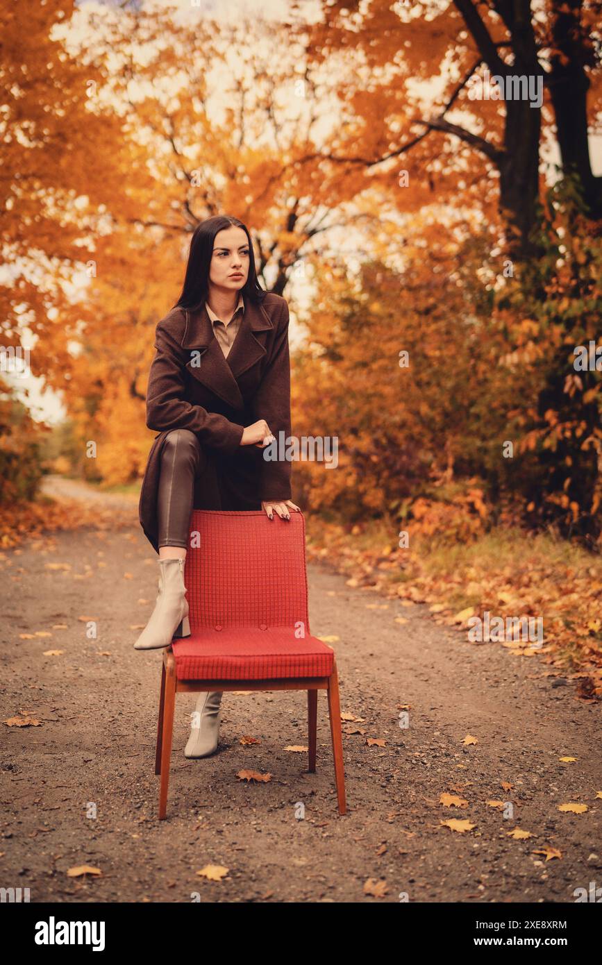 Portrait d'une jeune femme avec un vieux fauteuil dans un manteau brun en automne Banque D'Images