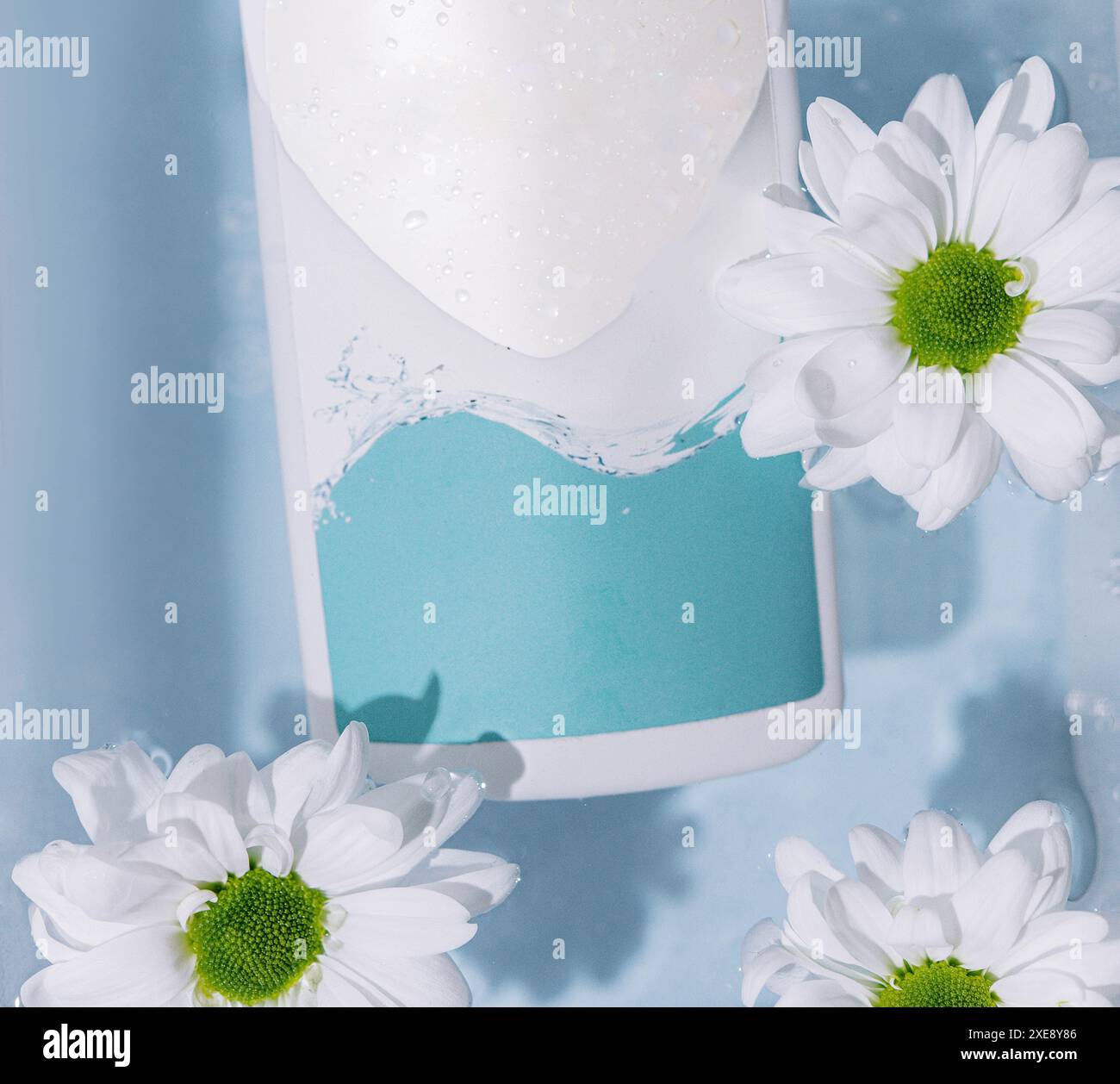 Shampooing ou produits de soins de la peau et fleurs de camomille sur une surface blanche avec de l'eau claire Banque D'Images