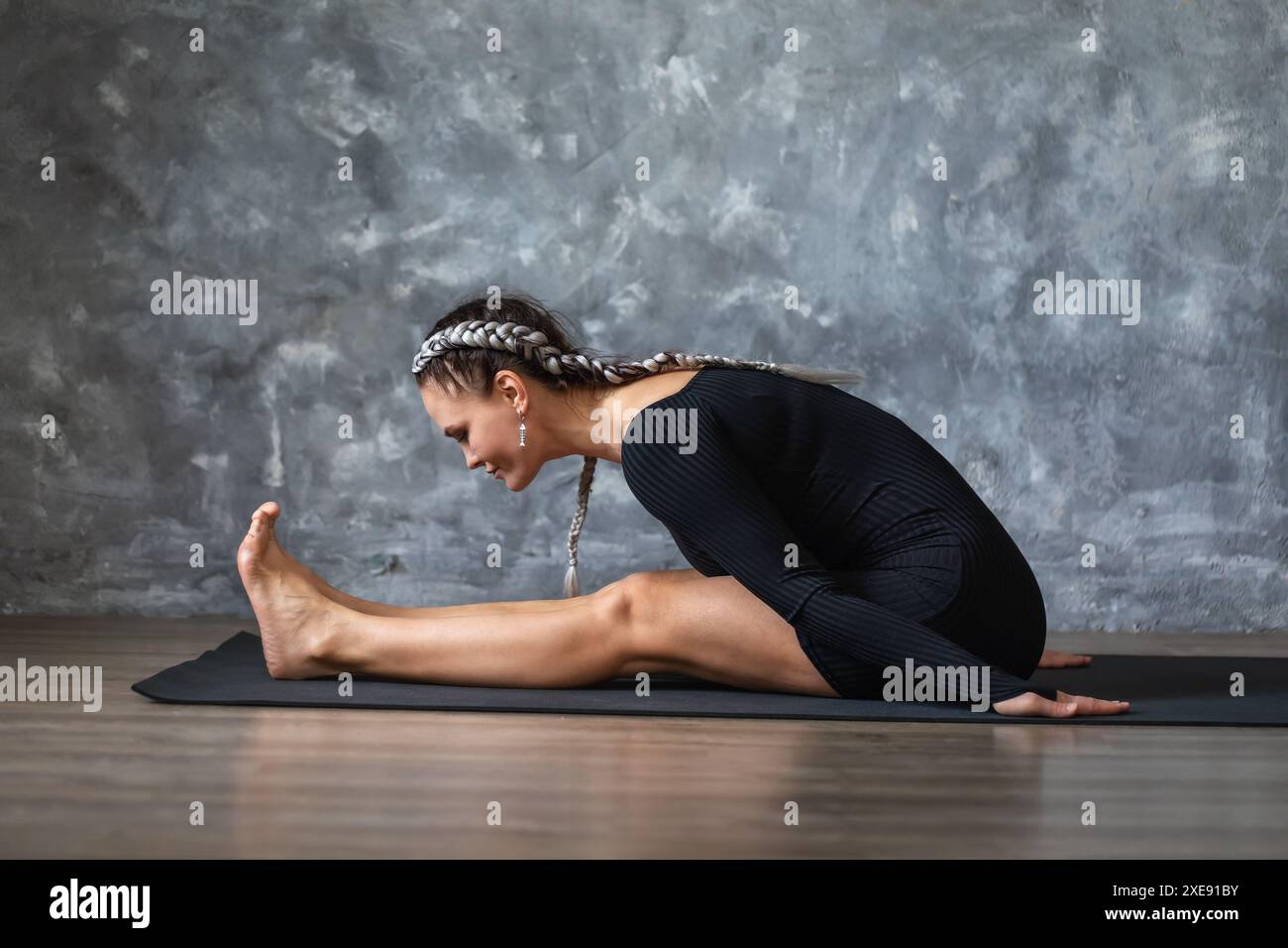 Une femme d'âge moyen effectue un exercice pour étirer les muscles de son dos et de ses jambes, se penche vers l'avant à partir d'une position assise, travaille en vêtements de sport o Banque D'Images