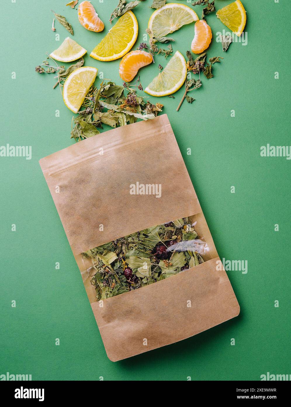 Thé en feuilles renversé hors d'un paquet de papier avec des tranches d'orange et de mandarine sur fond vert Banque D'Images Thé en feuilles renversé hors d'un paquet de papier avec des tranches d'orange et de mandarine sur fond vert Banque D'Images