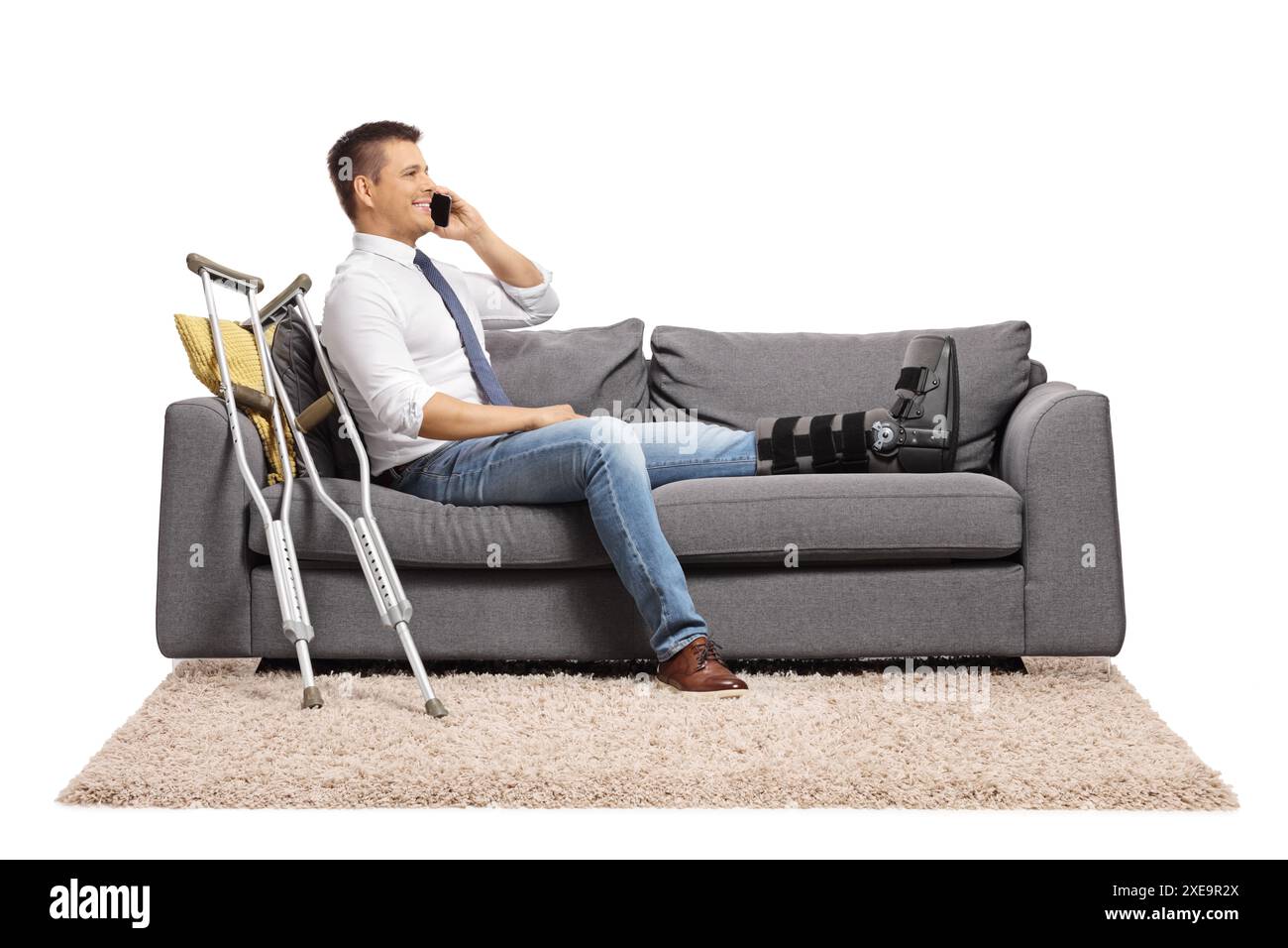 Hommes blessés avec une jambe cassée assis sur un canapé et utilisant un smartphone isolé sur fond blanc Banque D'Images