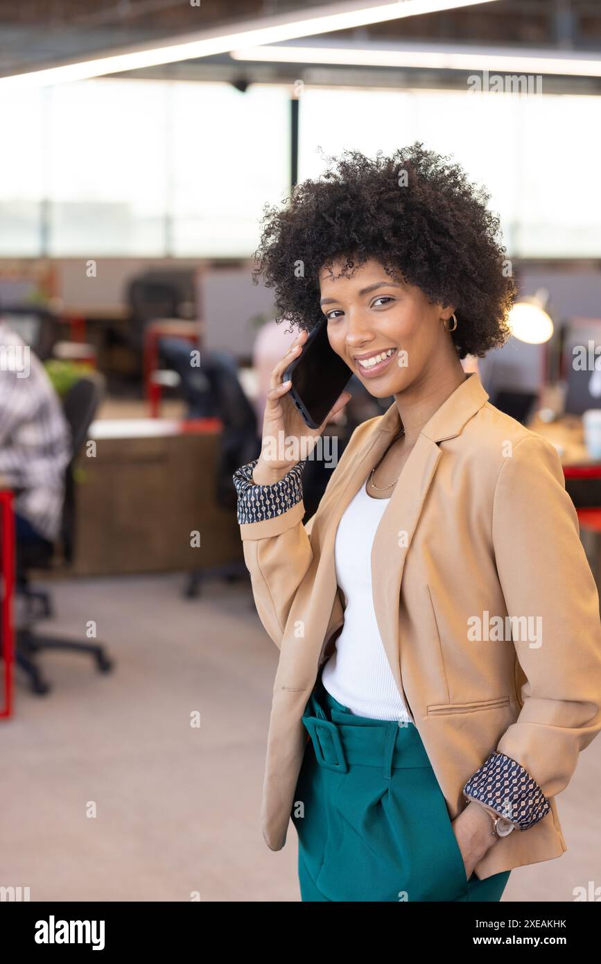 Tenant smartphone, souriante femme d'affaires afro-américaine debout dans un bureau moderne Banque D'Images