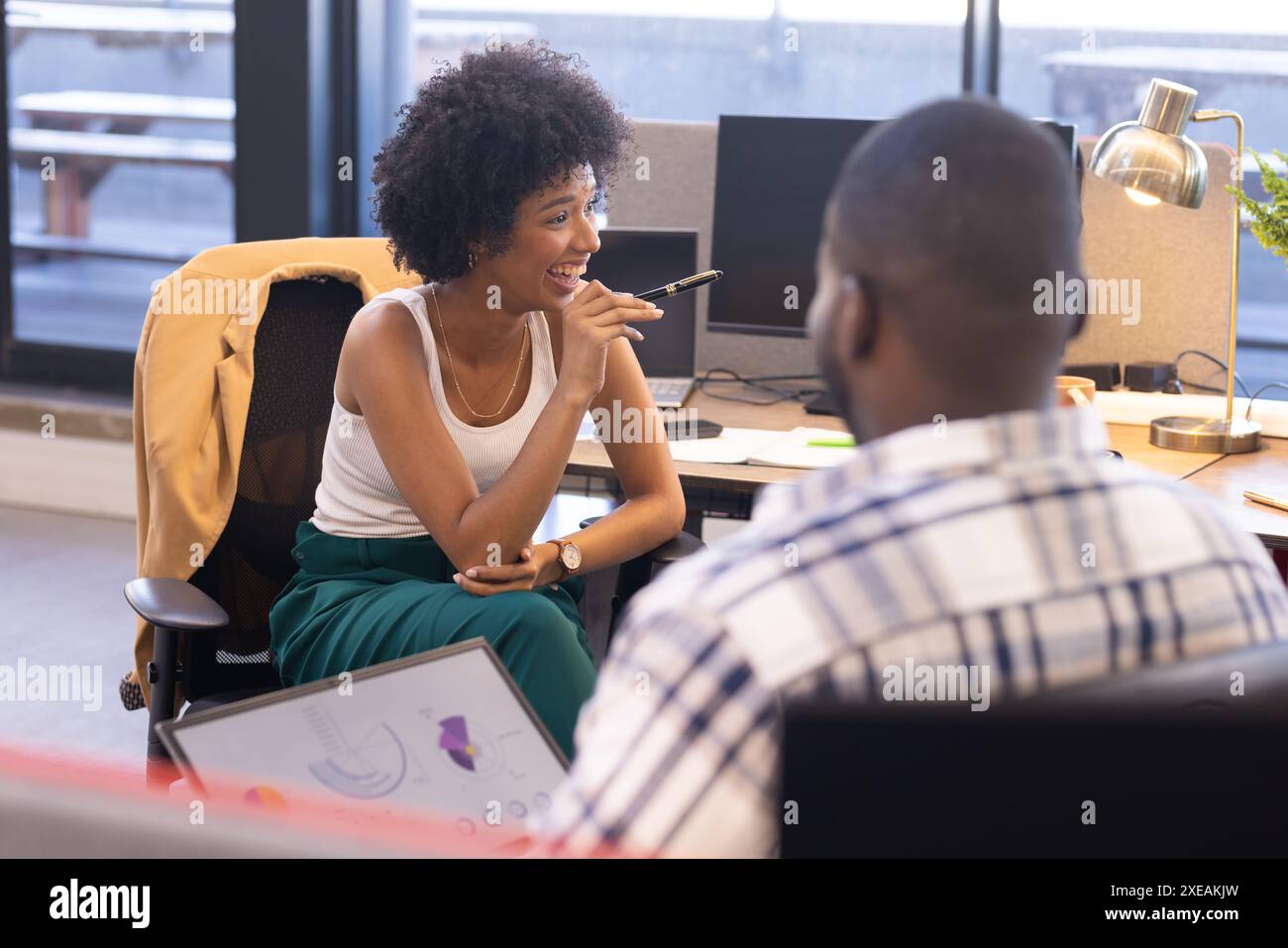 Femme d'affaires souriante tenant un stylo, discutant avec un collègue dans un bureau moderne Banque D'Images