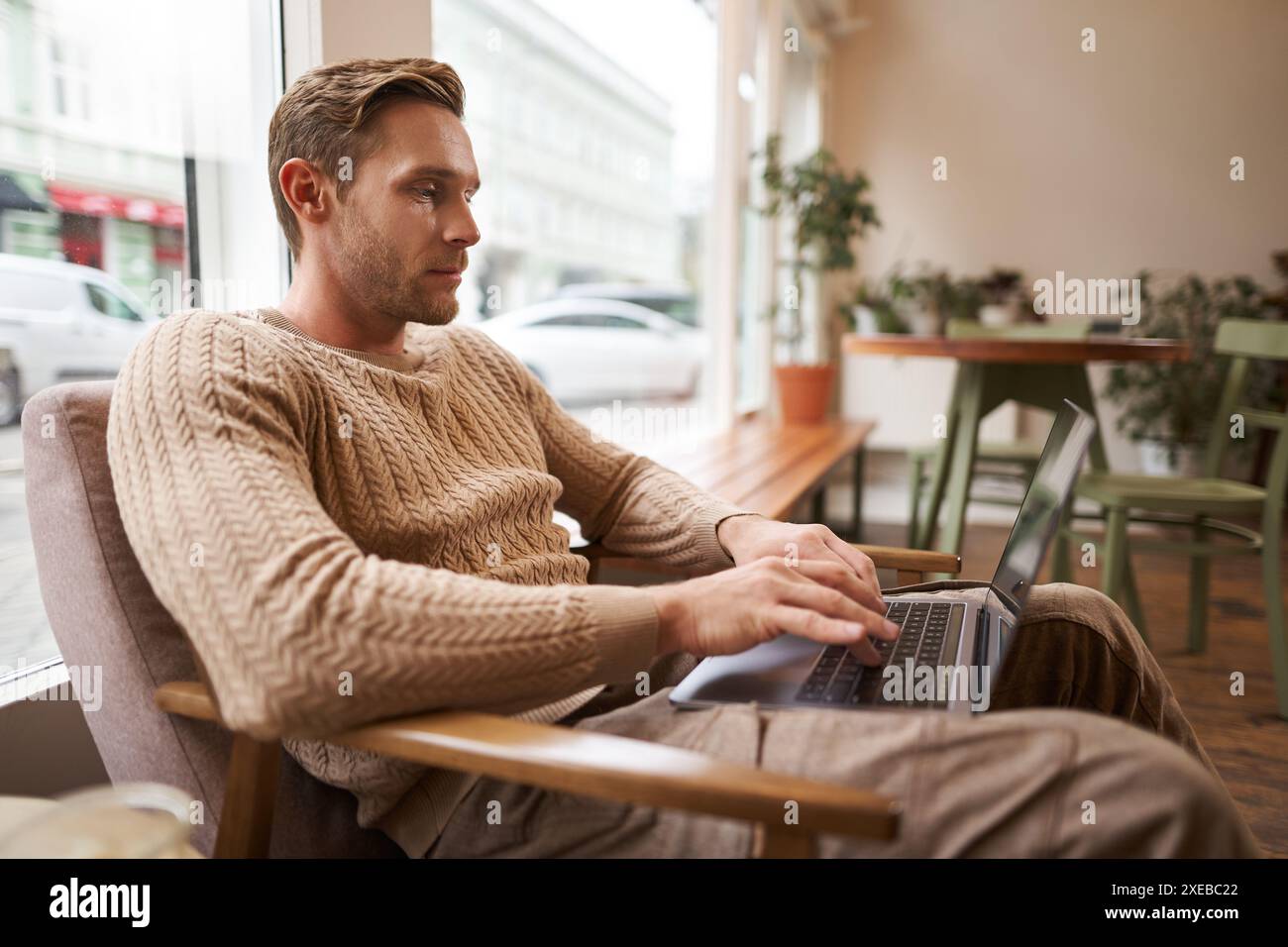 Personnes travailleuses et concept d'espace public. Jeune homme beau, ux ui designer assis avec un ordinateur portable dans un café, boire du cappuccino, lo Banque D'Images