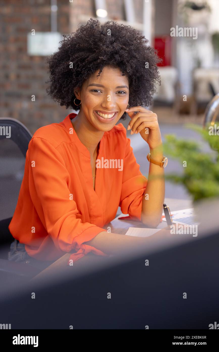 Femme d'affaires afro-américaine souriante en blouse orange travaillant au bureau dans le bureau Banque D'Images