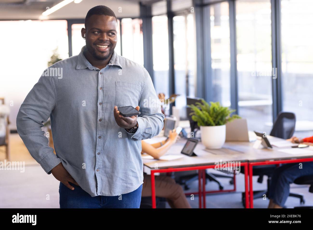 Tenant smartphone, homme d'affaires dans une tenue décontractée souriante dans un cadre de bureau moderne Banque D'Images